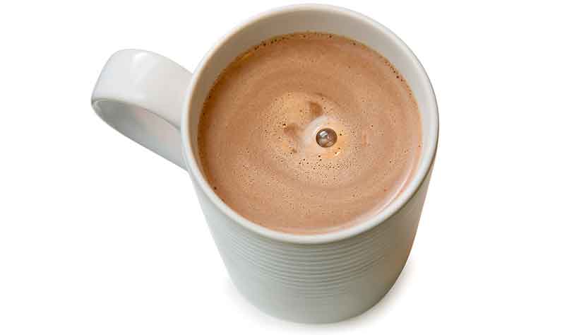Una taza de cocaína con chocolate caliente espumoso. Cacao en una pequeña taza blanca.