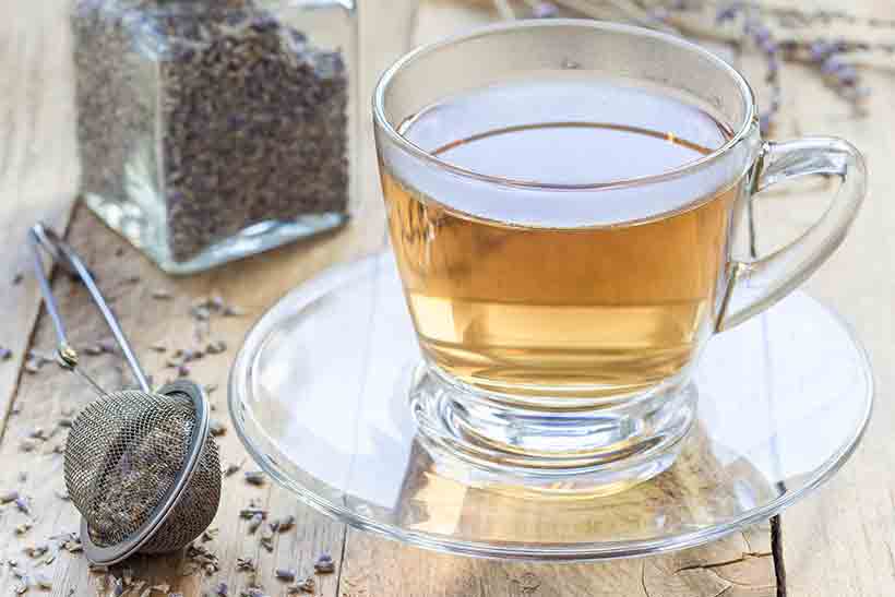 Vaso de té de lavanda junto a flores de lavanda secas. Té de lavanda en vaso sobre un escritorio.