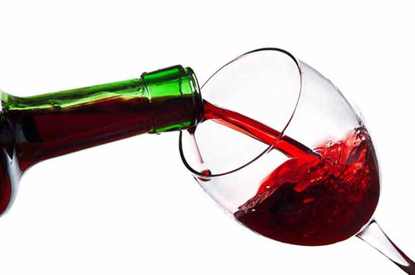 Vierta una copa de vino tinto. Verter una copa de vino tinto de una botella verde.