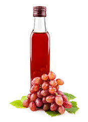 Botella de vinagre de vino tinto junto a algunas uvas rojas.