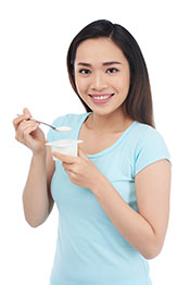 Mujer joven comiendo un pote de yogur.