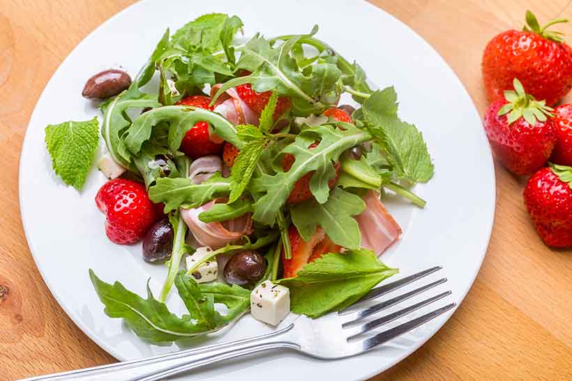 Ensalada griega que contiene jamón, fresa, queso feta, ensalada y aceitunas Kalamata.