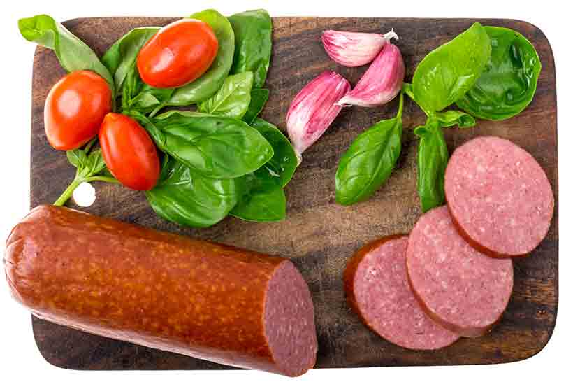 Salchichas de salami, chips de salami y verduras en una mesa de madera.