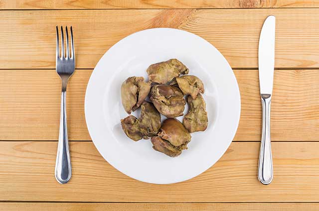 Trozos de hígado de pollo frito en un plato con cuchillo y tenedor.