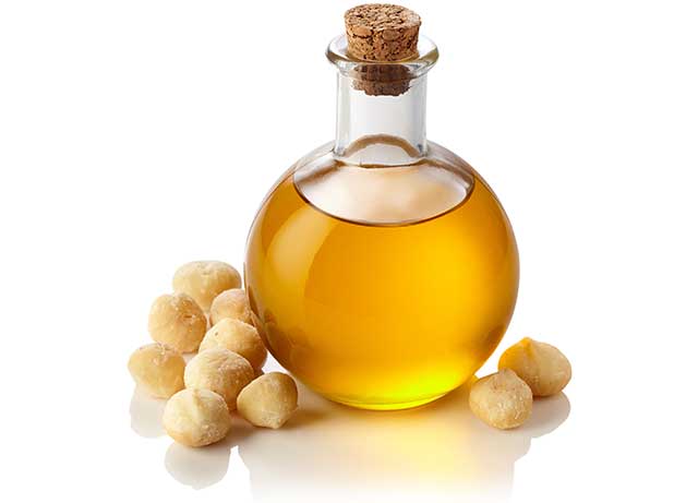 Aceite de macadamia en jarra de vidrio cerca de nueces de macadamia.