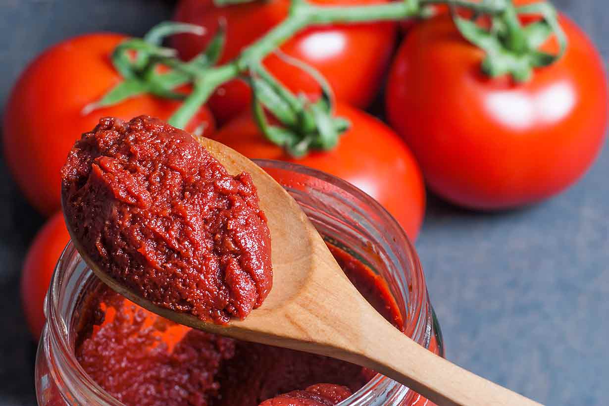 Pegar Tomates En Una Cuchara De Madera Con Tomates Enteros En El Fondo.