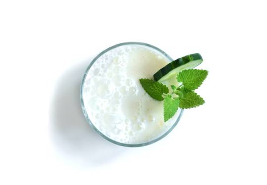 Yogur de bebida Ayran en un vaso con hoja de menta y rodaja de pepino.