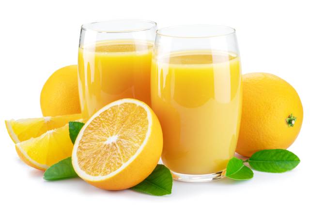 Naranjas enteras y medias naranjas junto a dos vasos de jugo de frutas.