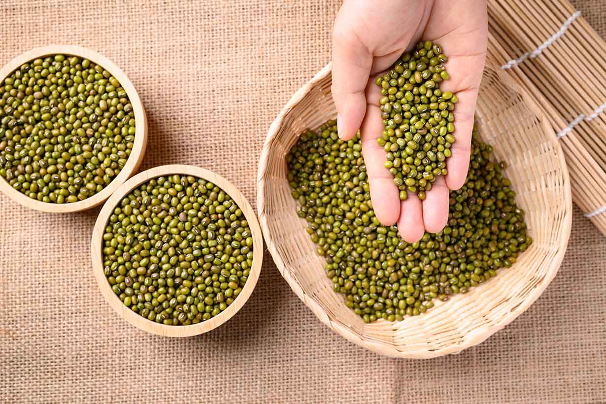 Frijoles mungo secos en un cuenco de paja y cuencos de madera.